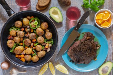 Ev yapımı yemekler, sebzeler, otlar, tavada kızarmış biftek ve yeni patateslerle dolu bir yemek masası.