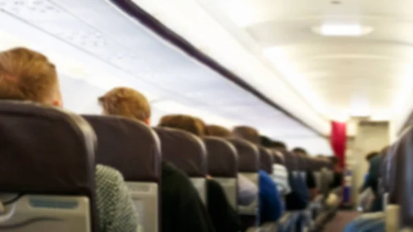 Blur background of passenger plane cabin with people sitting in armchairs, Plane travel concept