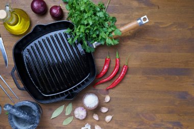 Ahşap desenli siyah demir tencere, baharatlar, barbekü sosu ve zeytinyağı..