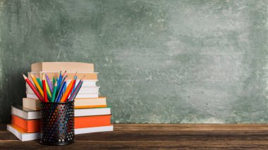 a Stack of books and stationery on the background of the school board. Education and back to school concept.
