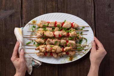 Grilled vegetable and chicken skewers with bell peppers, zucchini, onion and mushrooms on a wooden table in female hands, top view. Meat and vegetables kebabs on skewers.