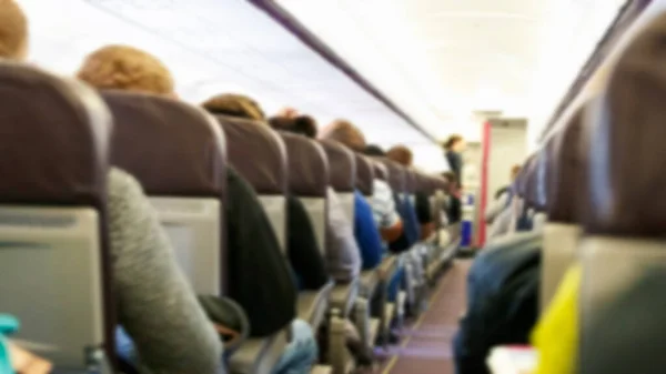 Blur background of passenger plane cabin with people sitting in armchairs, Plane travel concept