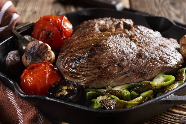 Large piece of grilled meat with vegetables in a cast iron pan, close-up, eating out, studio photo