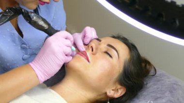 Kozmetik prosedürü. Kalıcı dudak makyajı. Güzellik uzmanı güzellik salonunda makyaj yapıyor.. 