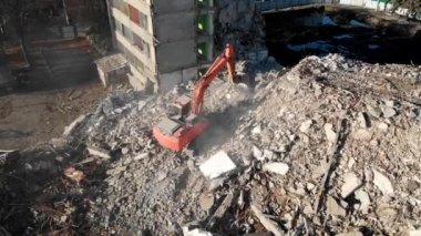 Bir kazıcı traktörü çökmüş bir evin beton kalıntılarını bir kovayla kazıyor..