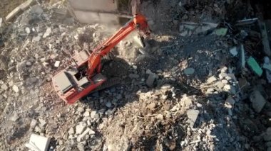 Bir kazıcı traktörü çökmüş bir evin beton kalıntılarını bir kovayla kazıyor..