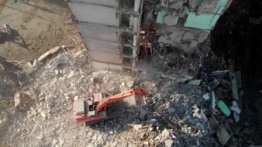 Bir kazıcı traktörü çökmüş bir evin beton kalıntılarını bir kovayla kazıyor..