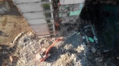 Bir kazıcı traktörü çökmüş bir evin beton kalıntılarını bir kovayla kazıyor..