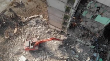 Bir kazıcı traktörü çökmüş bir evin beton kalıntılarını bir kovayla kazıyor..