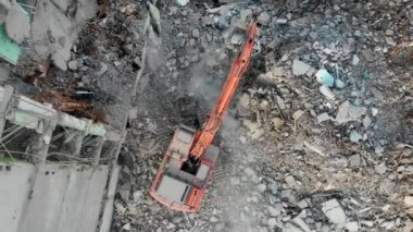 Bir kazıcı traktörü çökmüş bir evin beton kalıntılarını bir kovayla kazıyor..