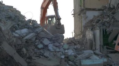 Bir kazıcı traktörü çökmüş bir evin beton kalıntılarını bir kovayla kazıyor..