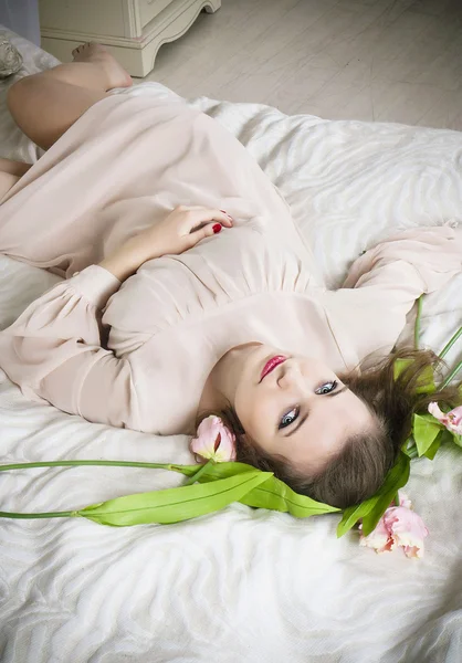 Mooie vrouw in roze jurk op het bed — Stockfoto