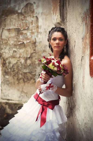 Bride with wedding bouquet leaning against the wall — Stock Photo, Image