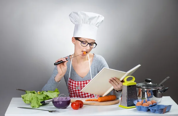 Pretty woman cooking with cookbook on gray background — Stock Photo, Image