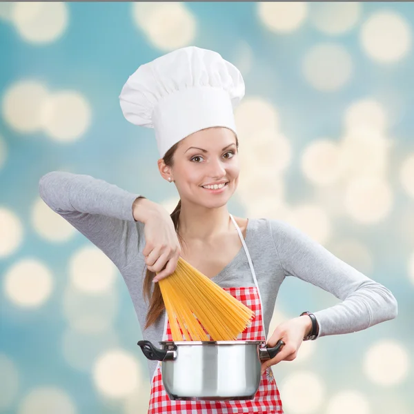 Femme souriante ajoutant les pâtes au pot, fond abstrait — Photo