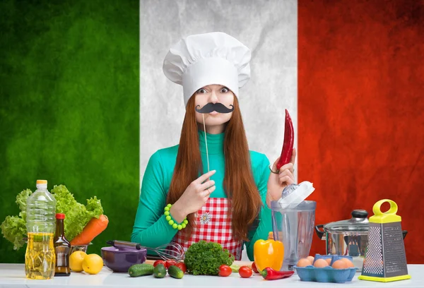 Funny female chef with paper mustache standing before an Italian flag