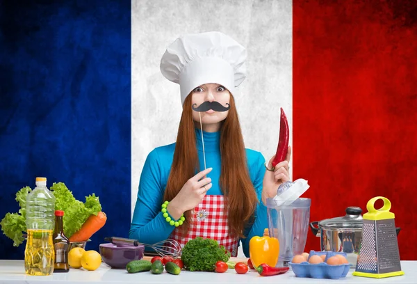 Chef feminino engraçado com bigode de papel em pé diante de uma bandeira da França — Fotografia de Stock