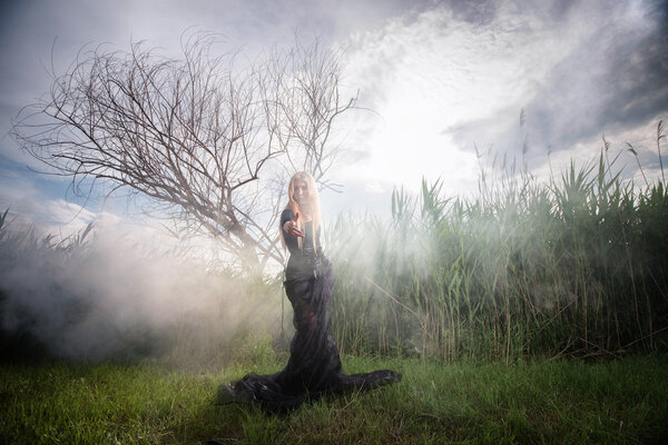 Weird female figure in black beckoning someone from the morning mist