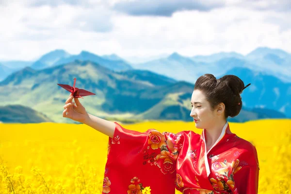 Geisha with an origami crane in the yellow flowering field — Stock Photo, Image