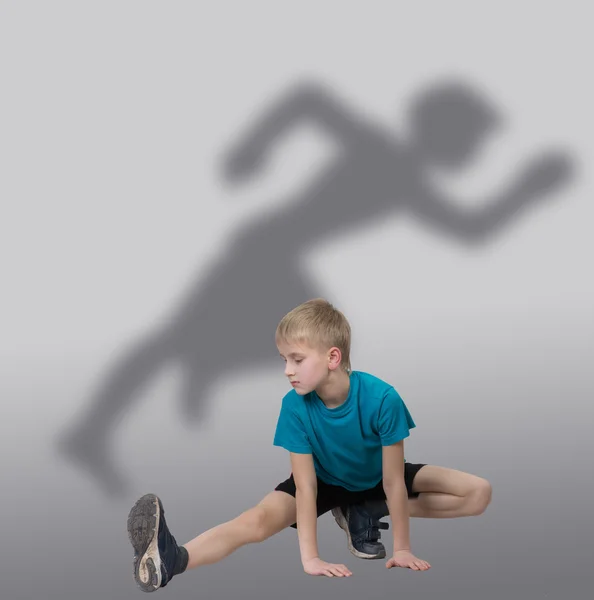 Menino esportivo esticando a perna com silhueta de corredor atrás dele — Fotografia de Stock
