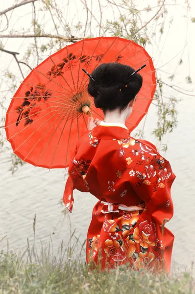 Geisha con paraguas rojo en la orilla del río (vista trasera ) — Foto de Stock