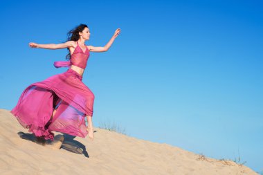 kum tepeleri üzerinde çalışan havadar koyu kırmızı elbiseli kız