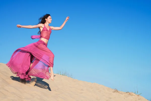 Meisje in luchtige crimson jurk draait op zandduinen — Stockfoto