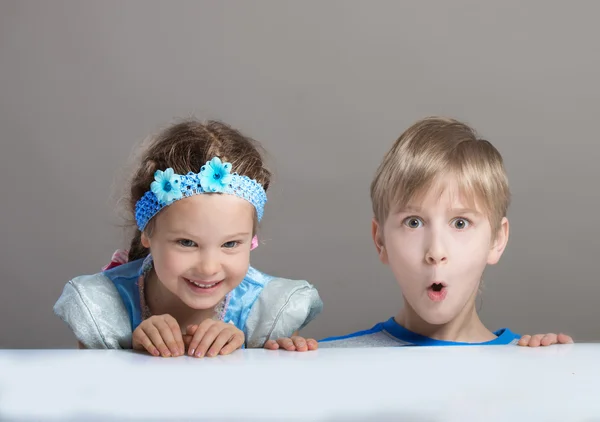 Crianças olhando para a câmera de trás da mesa — Fotografia de Stock