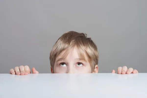 Garçon levant les yeux derrière la table — Photo