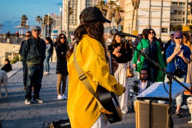 Tel Aviv, İsrail - Mart 06, 2022 Genç bağımsız şarkıcı Tel Aviv 'de denize bakan gezinti alanında bir müzik konseri veriyor, sanatçılar bu şekilde tanınıyor ve plaklarını aynı anda satıyorlar.
