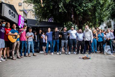 Tel Aviv, İsrail - 8 Nisan 2022 Dizengoff Caddesi 'ndeki Ilka Bar' a yapılan terörist saldırının ardından, genç İsrailli gençler saldırının gerçekleştiği yerde şarkı söylüyorlar.