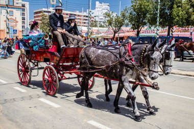 Seville, İspanya - 1 Mayıs 2022 Sevillianlar geleneksel Endülüs tarzında giyinmiş bir at arabasıyla İspanya 'nın en ünlü festivali olan Feria de Sevilla' nın koridorlarında dolaşıyorlar.