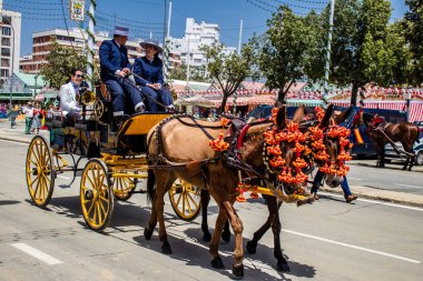 Seville, İspanya - 1 Mayıs 2022 Sevillianlar geleneksel Endülüs tarzında giyinmiş bir at arabasıyla İspanya 'nın en ünlü festivali olan Feria de Sevilla' nın koridorlarında dolaşıyorlar.