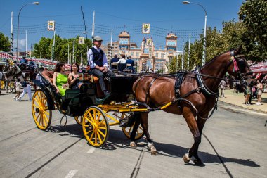 Seville, İspanya - 1 Mayıs 2022 Sevillianlar geleneksel Endülüs tarzında giyinmiş bir at arabasıyla İspanya 'nın en ünlü festivali olan Feria de Sevilla' nın koridorlarında dolaşıyorlar.