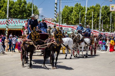 Seville, İspanya - 1 Mayıs 2022 Sevillianlar geleneksel Endülüs tarzında giyinmiş bir at arabasıyla İspanya 'nın en ünlü festivali olan Feria de Sevilla' nın koridorlarında dolaşıyorlar.