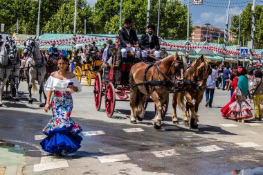 Seville, İspanya - 1 Mayıs 2022 Sevillianlar geleneksel Endülüs tarzında giyinmiş bir at arabasıyla İspanya 'nın en ünlü festivali olan Feria de Sevilla' nın koridorlarında dolaşıyorlar.