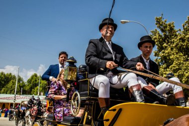 Seville, İspanya - 1 Mayıs 2022 Sevillianlar geleneksel Endülüs tarzında giyinmiş bir at arabasıyla İspanya 'nın en ünlü festivali olan Feria de Sevilla' nın koridorlarında dolaşıyorlar.
