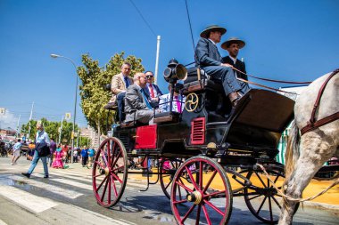 Seville, İspanya - 1 Mayıs 2022 Sevillianlar geleneksel Endülüs tarzında giyinmiş bir at arabasıyla İspanya 'nın en ünlü festivali olan Feria de Sevilla' nın koridorlarında dolaşıyorlar.