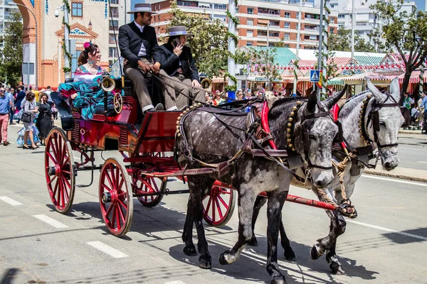 Seville, İspanya - 1 Mayıs 2022 Sevillianlar geleneksel Endülüs tarzında giyinmiş bir at arabasıyla İspanya 'nın en ünlü festivali olan Feria de Sevilla' nın koridorlarında dolaşıyorlar.