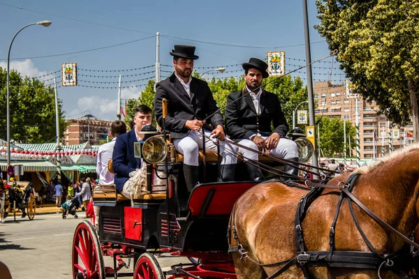 Seville, İspanya - 1 Mayıs 2022 Sevillianlar geleneksel Endülüs tarzında giyinmiş bir at arabasıyla İspanya 'nın en ünlü festivali olan Feria de Sevilla' nın koridorlarında dolaşıyorlar.
