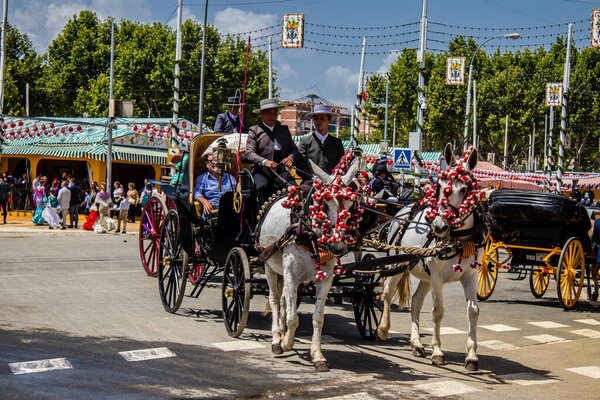 Севилья, Испания - 01 мая 2022 года Севилья, одетые в традиционный андалузский стиль верховой езды в конном экипаже через проходы Feria de Sevilla, самый известный фестиваль в Испании