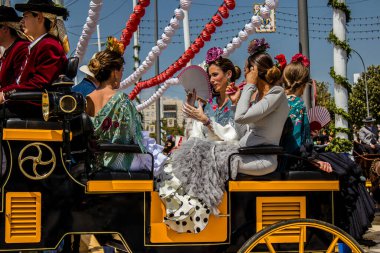 Seville, İspanya - 1 Mayıs 2022 Sevillianlar geleneksel Endülüs tarzında giyinmiş bir at arabasıyla İspanya 'nın en ünlü festivali olan Feria de Sevilla' nın koridorlarında dolaşıyorlar.