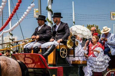 Seville, İspanya - 1 Mayıs 2022 Sevillianlar geleneksel Endülüs tarzında giyinmiş bir at arabasıyla İspanya 'nın en ünlü festivali olan Feria de Sevilla' nın koridorlarında dolaşıyorlar.