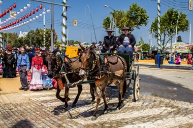 Seville, İspanya - 1 Mayıs 2022 Sevillianlar geleneksel Endülüs tarzında giyinmiş bir at arabasıyla İspanya 'nın en ünlü festivali olan Feria de Sevilla' nın koridorlarında dolaşıyorlar.