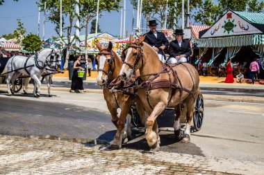 Seville, İspanya - 1 Mayıs 2022 Sevillianlar geleneksel Endülüs tarzında giyinmiş bir at arabasıyla İspanya 'nın en ünlü festivali olan Feria de Sevilla' nın koridorlarında dolaşıyorlar.