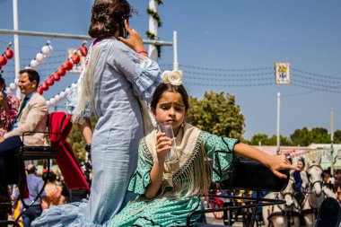 Seville, Spain - May 01, 2022 Sevillians dressed in the traditional Andalusian way riding in a horse drawn carriage through the aisles of the Feria de Sevilla, the most famous festival in Spain