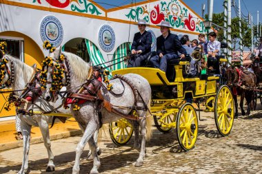 Seville, İspanya - 1 Mayıs 2022 Sevillianlar geleneksel Endülüs tarzında giyinmiş bir at arabasıyla İspanya 'nın en ünlü festivali olan Feria de Sevilla' nın koridorlarında dolaşıyorlar.
