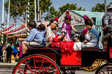 Seville, İspanya - 1 Mayıs 2022 Sevillianlar geleneksel Endülüs tarzında giyinmiş bir at arabasıyla İspanya 'nın en ünlü festivali olan Feria de Sevilla' nın koridorlarında dolaşıyorlar.