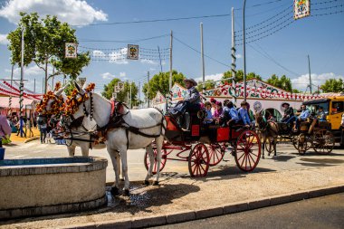 Seville, İspanya - 1 Mayıs 2022 Sevillianlar geleneksel Endülüs tarzında giyinmiş bir at arabasıyla İspanya 'nın en ünlü festivali olan Feria de Sevilla' nın koridorlarında dolaşıyorlar.