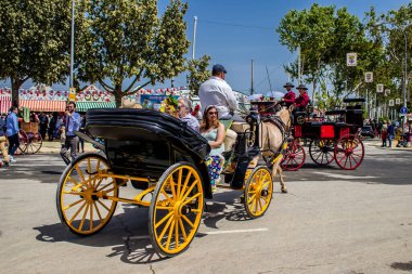 Seville, İspanya - 1 Mayıs 2022 Sevillianlar geleneksel Endülüs tarzında giyinmiş bir at arabasıyla İspanya 'nın en ünlü festivali olan Feria de Sevilla' nın koridorlarında dolaşıyorlar.